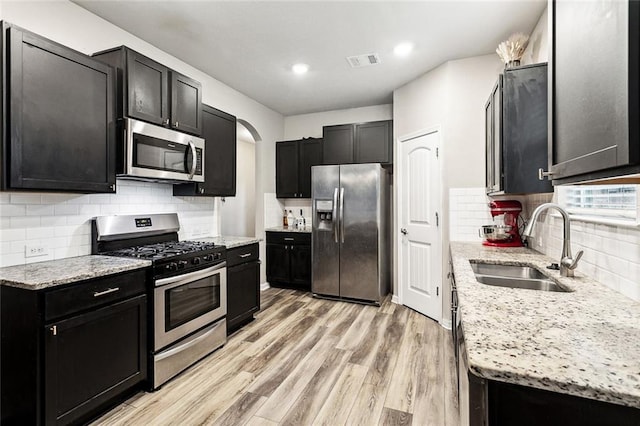 kitchen featuring stainless steel appliances, a sink, dark cabinetry, tasteful backsplash, and recessed lighting