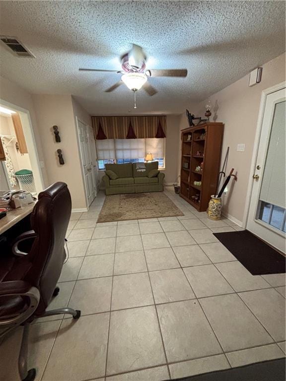 living room with ceiling fan, a textured ceiling, light tile patterned floors, and a desk