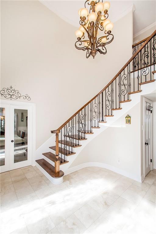 stairs with a towering ceiling, a chandelier, french doors, and baseboards
