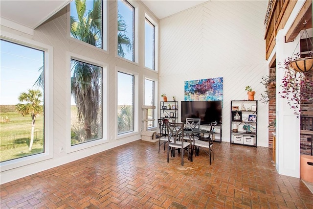 sunroom with plenty of natural light, a towering ceiling, brick flooring, and wooden walls