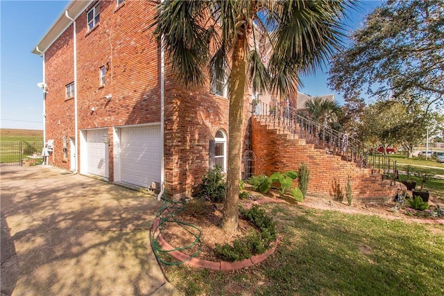 view of home's exterior featuring concrete driveway, brick siding, a garage, and stairway