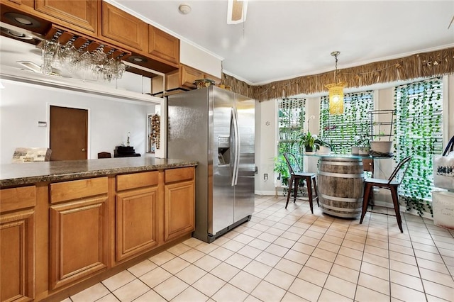 kitchen featuring stainless steel fridge with ice dispenser, light tile patterned floors, brown cabinetry, crown molding, and dark countertops