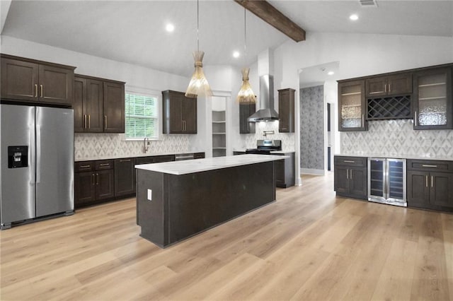 kitchen featuring appliances with stainless steel finishes, beverage cooler, light countertops, wall chimney exhaust hood, and dark brown cabinetry