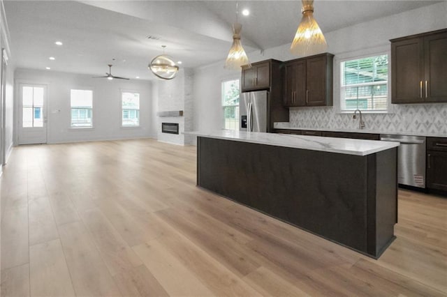 kitchen featuring appliances with stainless steel finishes, dark brown cabinets, a center island, light wood finished floors, and decorative backsplash