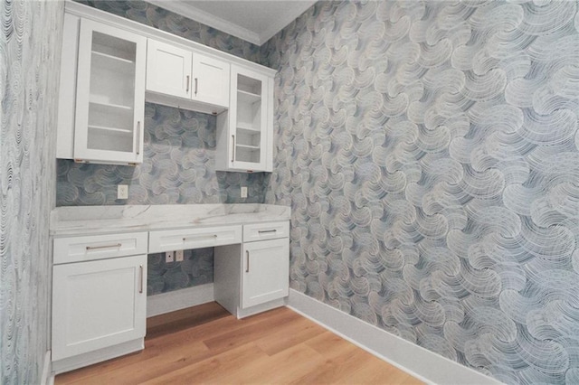 unfurnished office with wallpapered walls, light wood-style flooring, built in study area, ornamental molding, and baseboards