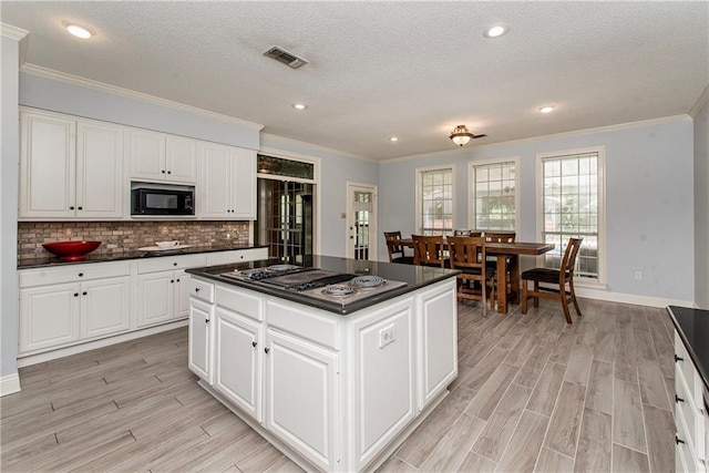 412 Magnolia Ln, Slidell, LA 70461 - kitchen with stovetop with downdraft, dark countertops, black microwave, crown molding, and light wood-style floors