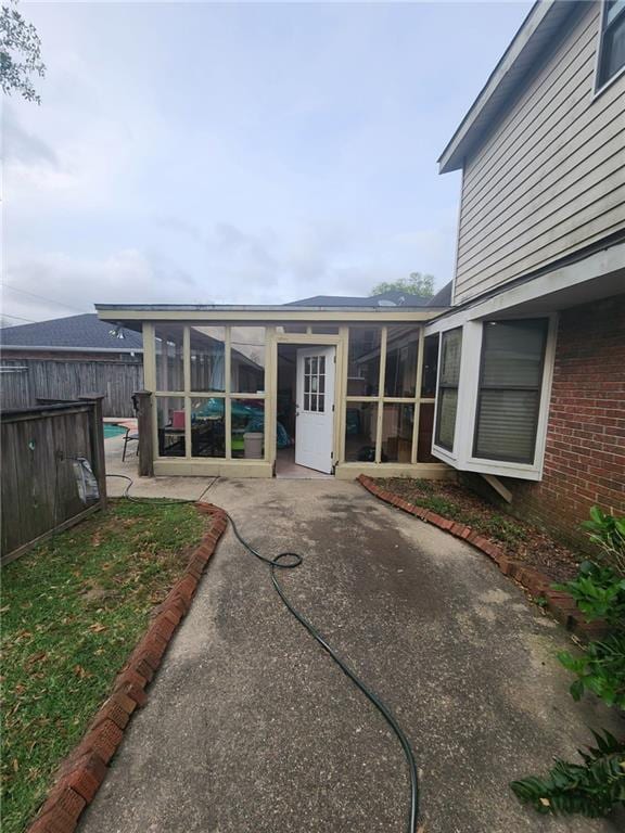 rear view of property featuring a sunroom, a patio, fence, and brick siding
