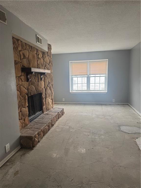 unfurnished living room with a textured ceiling, a stone fireplace, and baseboards