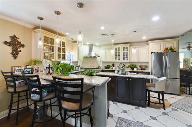 510 Nursery Ave, Metairie, LA 70005 - kitchen featuring freestanding refrigerator, wall chimney range hood, a breakfast bar, a peninsula, and light stone countertops