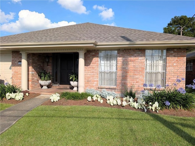 view of front facade with a shingled roof, a front yard, and brick siding