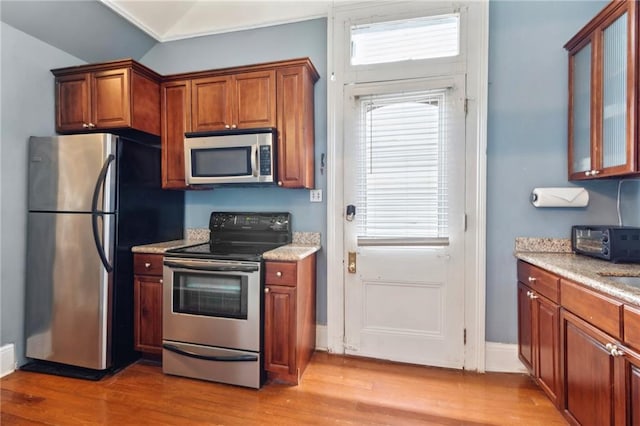 1614 Governor Nicholls St Unit 1, New Orleans, LA 70116 - kitchen with stainless steel appliances, light wood-style floors, brown cabinetry, lofted ceiling, and light stone counters