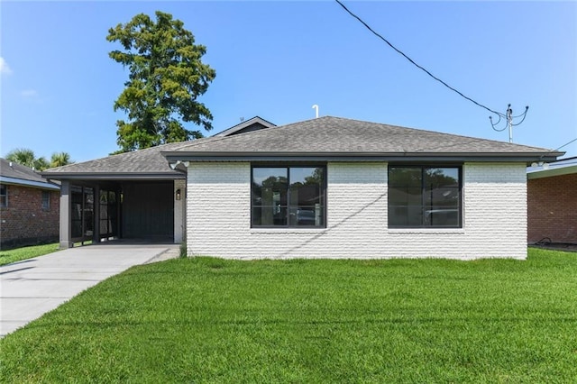 view of front of home with brick siding, concrete driveway, a front yard, a shingled roof, and an attached carport