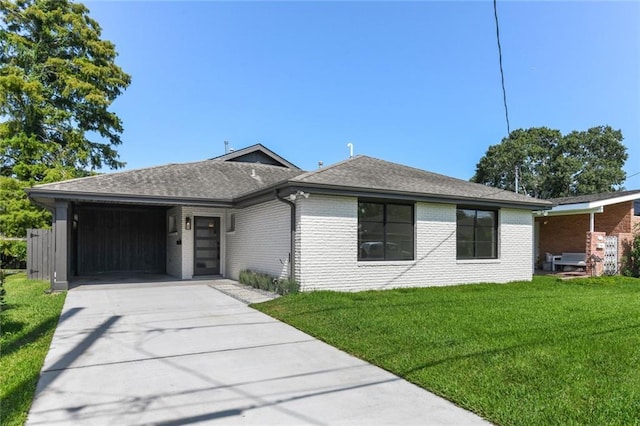 ranch-style home with concrete driveway, a front yard, roof with shingles, and brick siding