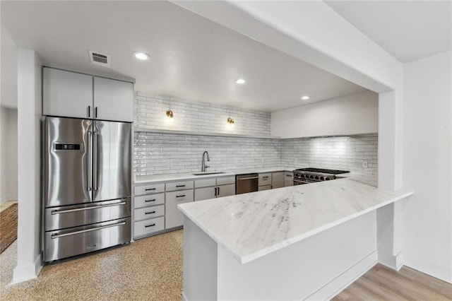kitchen with appliances with stainless steel finishes, a sink, a peninsula, tasteful backsplash, and baseboards