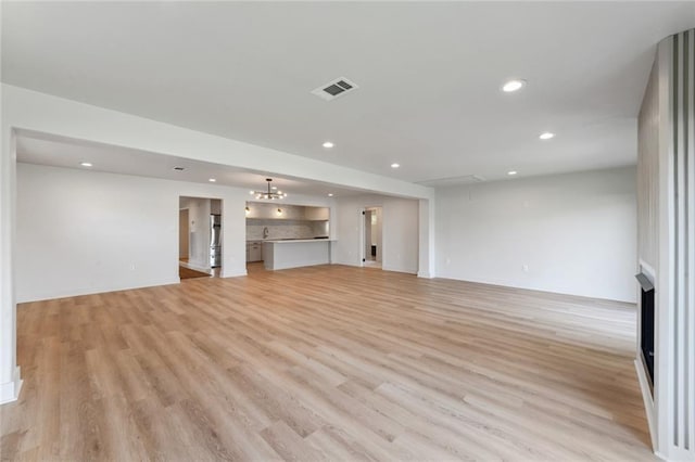 unfurnished living room featuring recessed lighting, light wood-type flooring, baseboards, and attic access