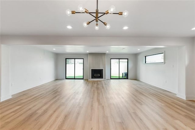 unfurnished living room with a chandelier, healthy amount of natural light, light wood-style floors, baseboards, and recessed lighting