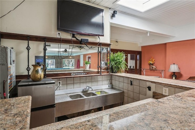 922 Lamanche St, New Orleans, LA 70117 - kitchen with beam ceiling, a skylight, tasteful backsplash, a sink, and stone counters