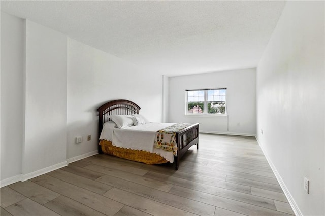 bedroom with light wood-style flooring, baseboards, and a textured ceiling
