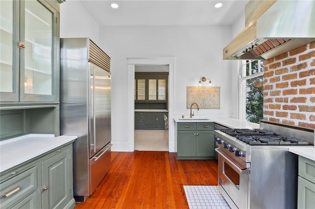 1631 State St, New Orleans, LA 70118 - kitchen featuring premium appliances, wall chimney range hood, a sink, light countertops, and green cabinets