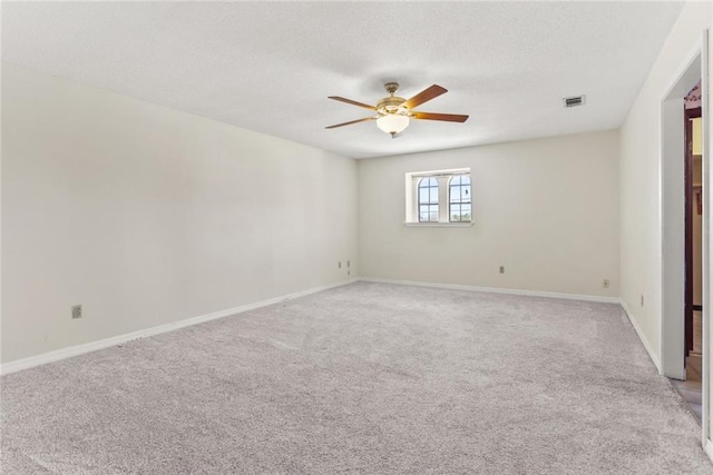empty room featuring ceiling fan, light colored carpet, baseboards, and a textured ceiling