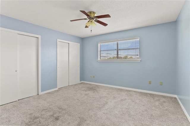 unfurnished bedroom with two closets, carpet floors, baseboards, a textured ceiling, and ceiling fan