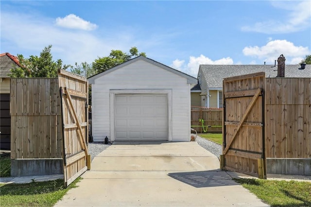 detached garage with a gate, concrete driveway, and fence