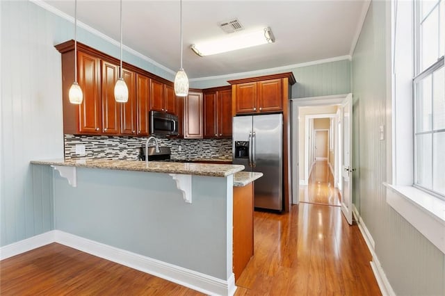 525 S Telemachus St, New Orleans, LA 70119 - kitchen featuring stainless steel appliances, a peninsula, a kitchen breakfast bar, light wood finished floors, and backsplash