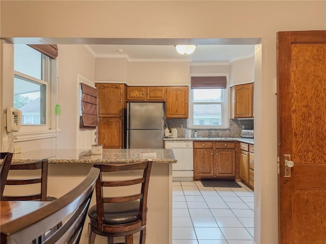 28 San Jose Ave, Jefferson, LA 70121 - kitchen featuring freestanding refrigerator, dishwasher, brown cabinetry, a kitchen bar, and light stone counters