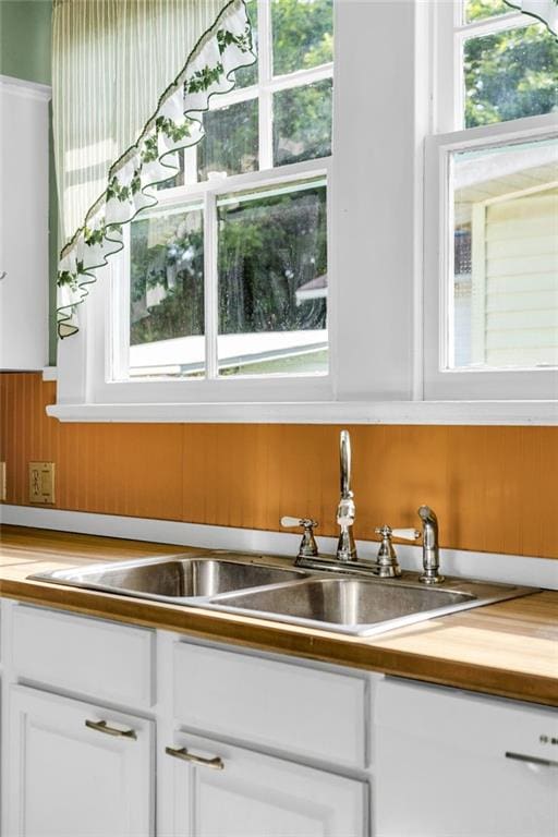 2437 Jonquil St, New Orleans, LA 70122 - kitchen with plenty of natural light, white cabinets, butcher block countertops, a sink, and a wainscoted wall