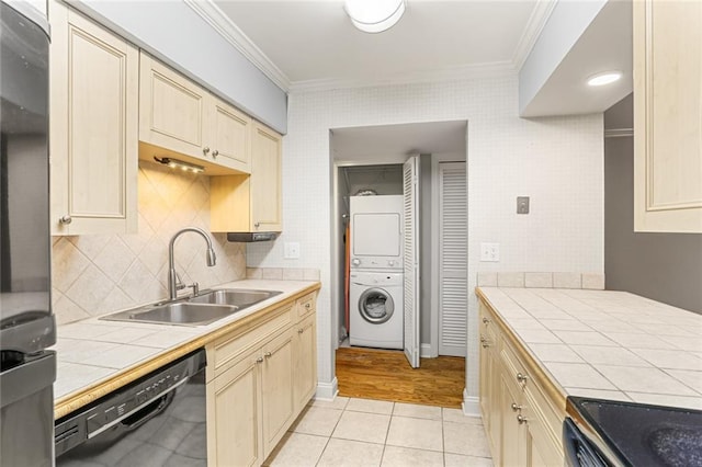 kitchen with stacked washer / drying machine, a sink, black dishwasher, tile countertops, and ornamental molding