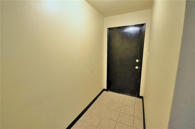 doorway with a textured ceiling, baseboards, and light tile patterned floors