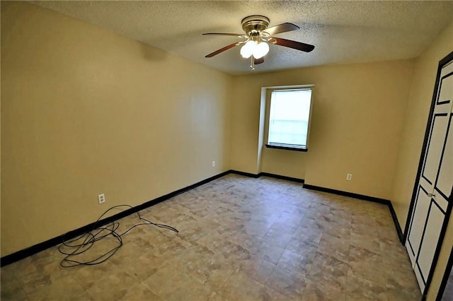 empty room with a textured ceiling, a ceiling fan, and baseboards