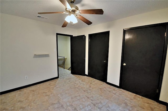 unfurnished bedroom featuring two closets, a textured ceiling, baseboards, and a ceiling fan
