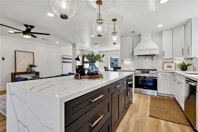 5116 Wilson Dr, Metairie, LA 70003 - kitchen with custom range hood, appliances with stainless steel finishes, light wood finished floors, recessed lighting, and white cabinetry