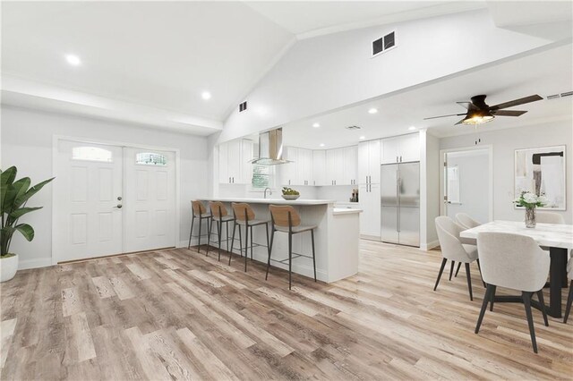 400 Sophia St, River Ridge, LA 70123 - kitchen with built in fridge, wall chimney exhaust hood, a peninsula, a kitchen breakfast bar, and white cabinetry