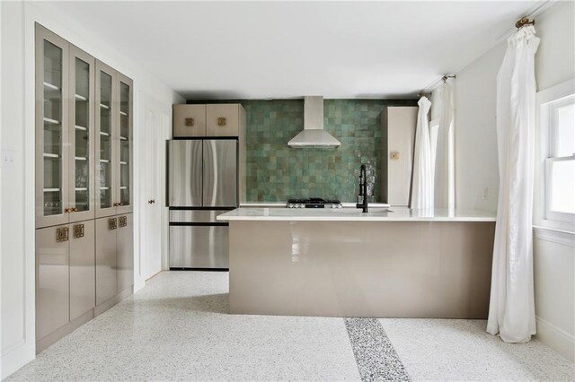 1729 Prytania St, New Orleans, LA 70130 - kitchen featuring stainless steel fridge, wall chimney exhaust hood, tasteful backsplash, glass insert cabinets, and speckle patterned floor