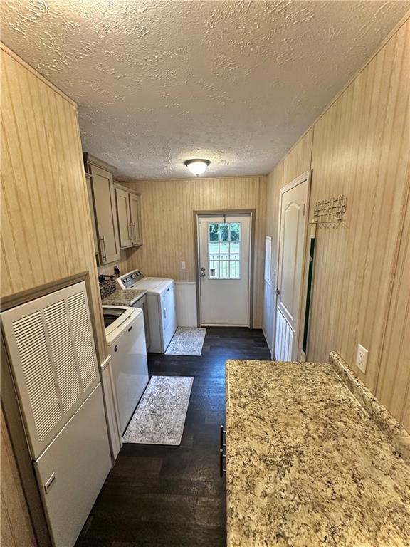 40140 Fire Tower Rd, Ponchatoula, LA 70454 - clothes washing area with washer and clothes dryer, cabinet space, dark wood-style flooring, wooden walls, and a textured ceiling
