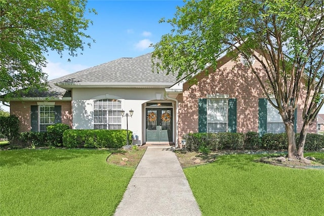 101 Portrush Dr, La Place, LA 70068 - view of front facade featuring french doors, a front lawn, roof with shingles, brick siding, and stucco siding