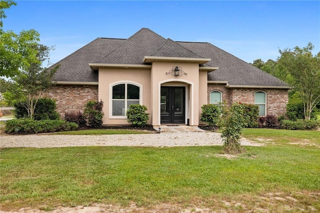 french country style house featuring french doors, a front yard, roof with shingles, and brick siding