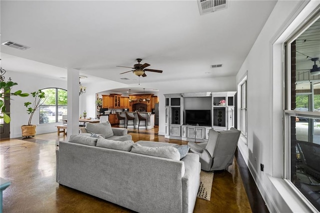 living area featuring a ceiling fan, arched walkways, finished concrete floors, and a chandelier