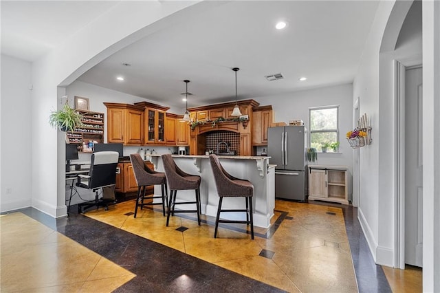 kitchen featuring freestanding refrigerator, brown cabinets, a breakfast bar area, recessed lighting, and an island with sink