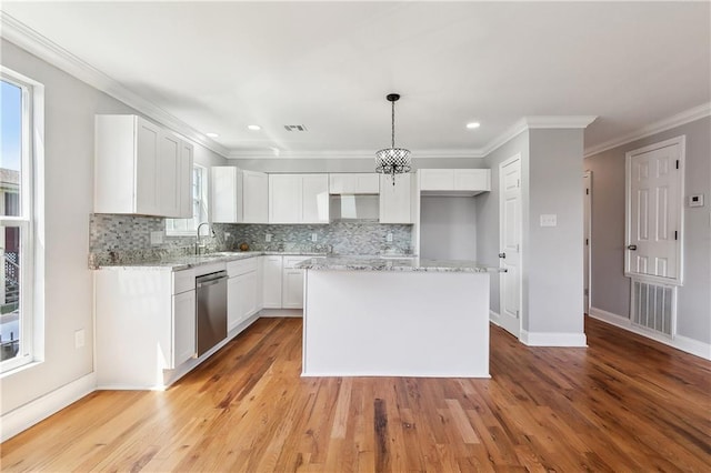 kitchen featuring stainless steel dishwasher, backsplash, a center island, a sink, and white cabinetry