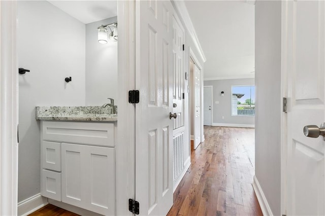 corridor featuring dark wood-type flooring, crown molding, baseboards, and a sink