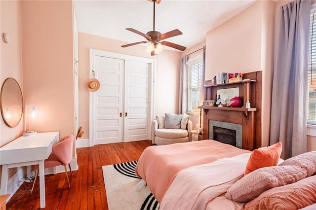 bedroom featuring hardwood / wood-style floors, a fireplace, a closet, baseboards, and a ceiling fan
