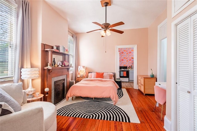 bedroom with multiple windows, wood finished floors, a closet, and a fireplace