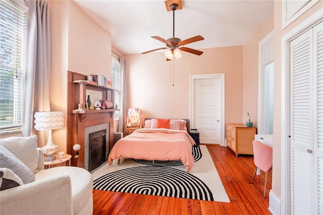bedroom with multiple windows, wood finished floors, a closet, and a fireplace