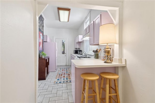 kitchen with freestanding refrigerator, a kitchen bar, light countertops, a peninsula, and range