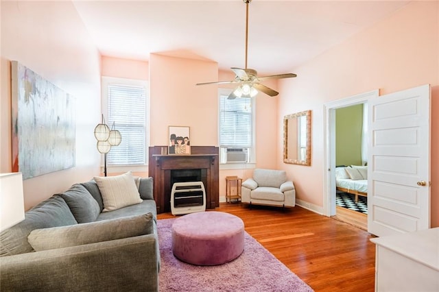 living area with wood finished floors, ceiling fan, cooling unit, baseboards, and a fireplace