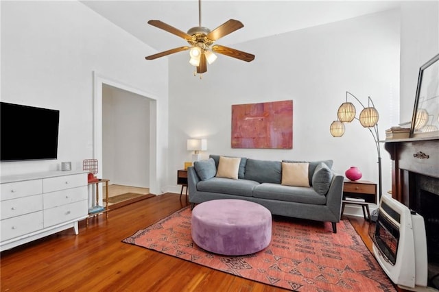 living room with heating unit, wood finished floors, a ceiling fan, a fireplace, and high vaulted ceiling