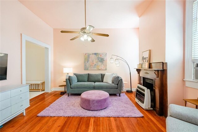 living room featuring heating unit, wood finished floors, a ceiling fan, and a fireplace